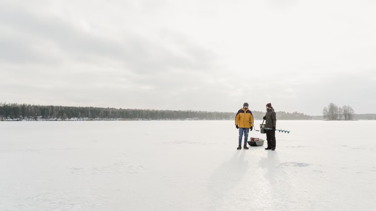 Two people ice fishing on a snow-covered frozen lake in winter.